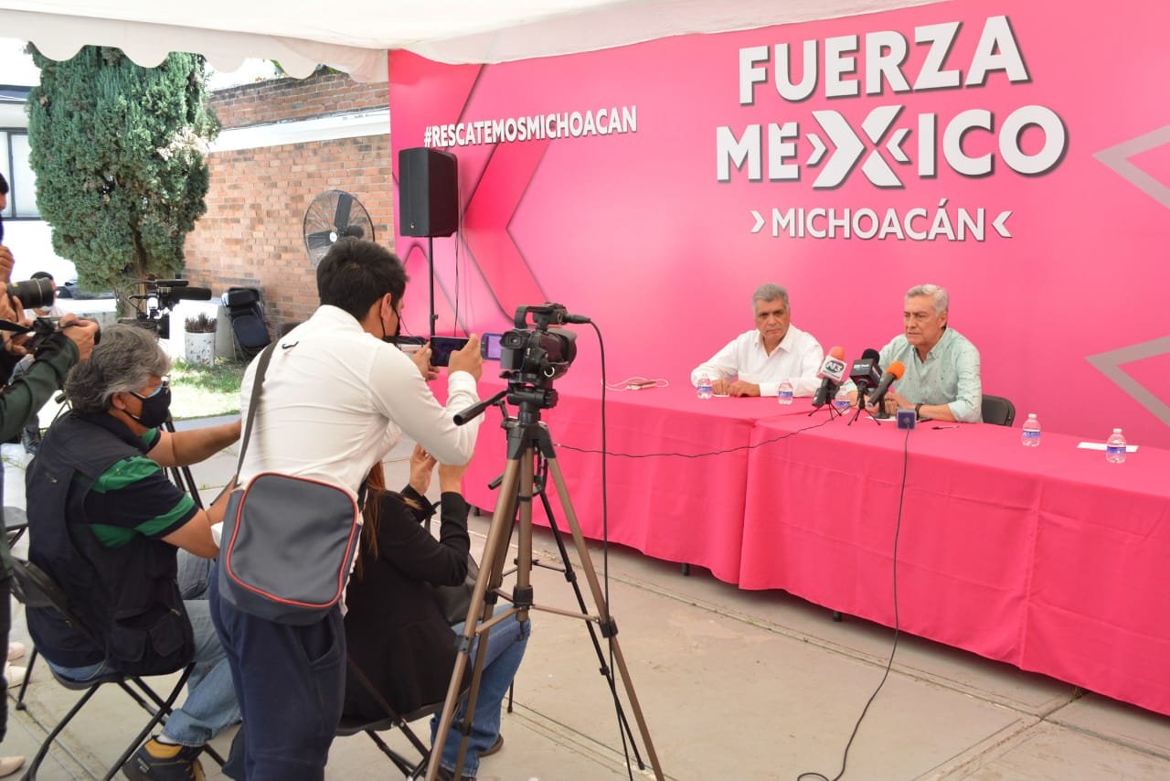 Cistobal Arias dando una conferencia para personal de la prensa de distintos medios en una mesa rosa y con todo un escenario rosa