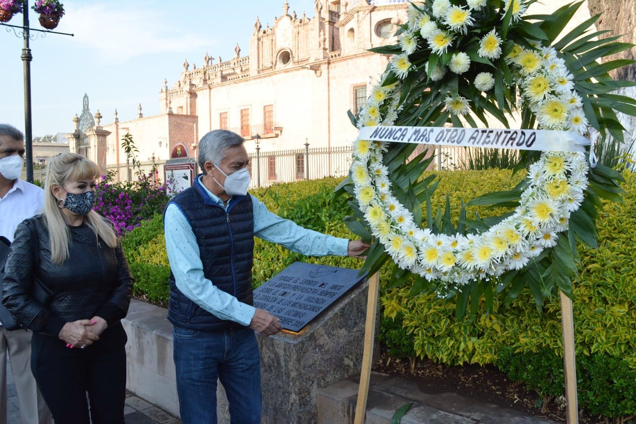 Cristóbal Arias posa para fotografía en placa conmemorativa del atentado de hace 13 años en la celebración de la independencia en Morelia acomodando una corona de flores