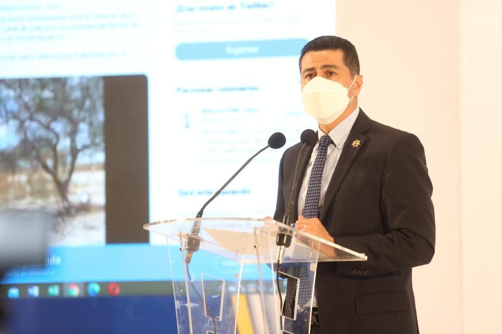 Secretario de Seguridad de Michoacán Israel Patrón en dando un discurso con una pantalla mostrando un video a sus espaldas
