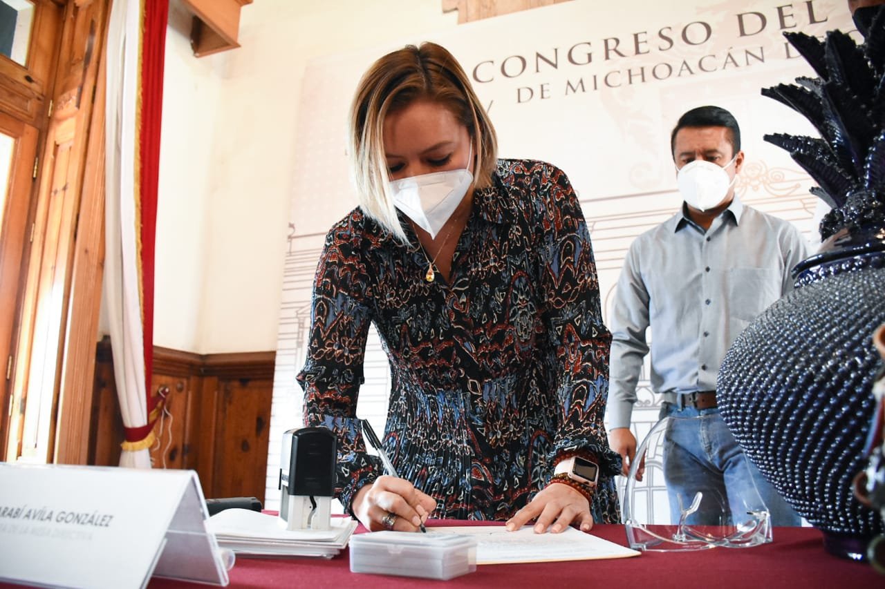 La guapa diputada Yarabí Ávila firma un documento de pie reclinada sobre una mesa