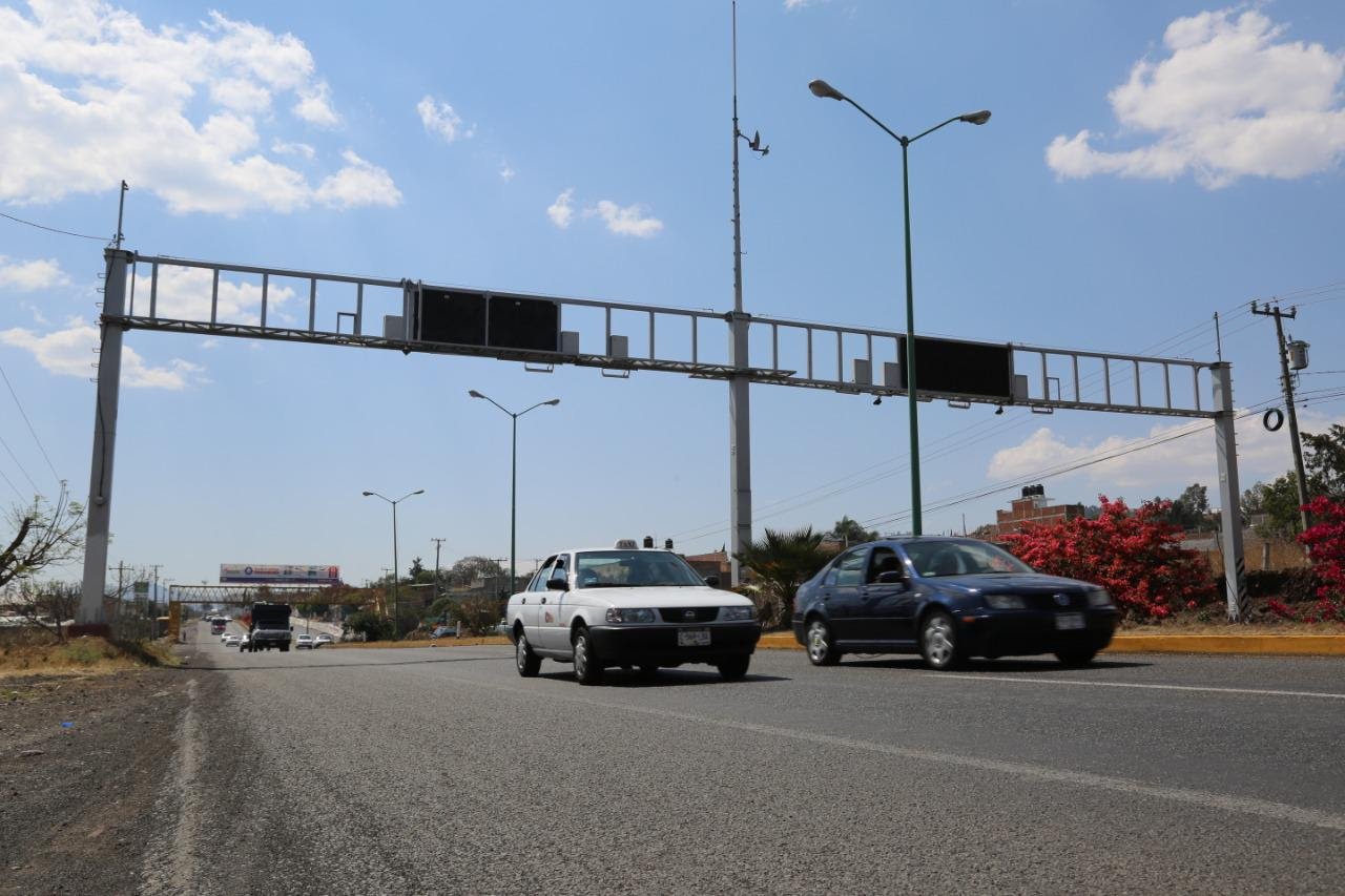 Dos vehiculos que circulan en una avenida donde hay cámaras de vigilancia