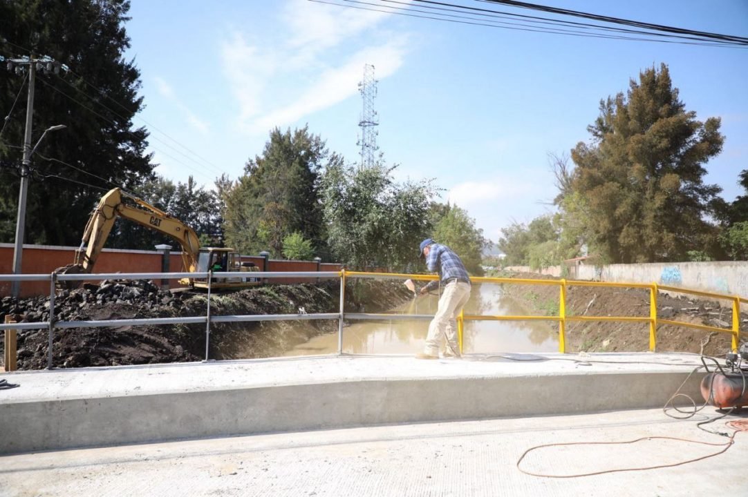 Cerca de 150 trabajadores municipales, han laborado día y noche en la construcción del mismo. Morelia, Michoacán; a 20 de junio de 2022.- A una semana del socavón en el puente del dren Barajas, en la avenida Siervo de la Nación, la construcción de uno nuevo, seguro y de calidad, como lo instruyó el presidente municipal, Alfonso Martínez Alcázar, presenta un avance de 95%, informó el secretario de Obras Públicas, Juan Fernando Sosa Tapia. “Somos 150 personas las que hemos estado día y noche en estos trabajos. Hay geólogos, hay hidrólogos, están los estructuristas, topógrafos y vamos a la par; estamos trabajando en lo técnico, en lo administrativo y operativo. Hoy es un día muy especial porque se cumple una semana del acontecimiento y estamos haciendo todo para concluir lo más pronto posible”, dijo Sosa Tapia. El secretario externó que este lunes se está trabajando en los aproches, el remate entre la loza de concreto y la vialidad de Siervo de la Nación, y finalmente se espera la prueba de laboratorio, misma que debe arrojar que el concreto ya tenga la resistencia máxima y con ello, se procede a la apertura de la vialidad. “El presidente Alfonso Martínez nos ha dado todos los elementos necesarios, porque las y los morelianos no deben sufrir por estas contingencias y nos instruye a que Morelia siga brillando, a través de este trabajo interinstitucional”, añadió el funcionario municipal. Agregó que esta obra beneficiará a cerca de 5 mil personas, que es el aproximado de quienes convergen en esta zona, aunque será una vialidad para el uso de todas y todos los morelianos. “Hoy colocaremos el concreto asfáltico, los barandales, las rampas para personas con discapacidad, porque el alcalde nos ha pedido que sea un proyecto incluyente; posteriormente procederemos con temas de limpieza, balizamiento, entre otros”, finalizó el secretario de Obras Públicas.